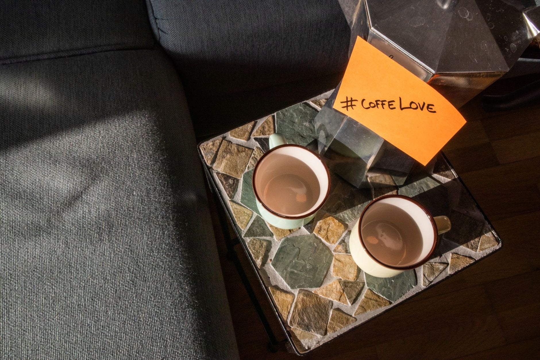 Warm morning sunlight on a coffee setup with Moka pot and cups on a mosaic table.